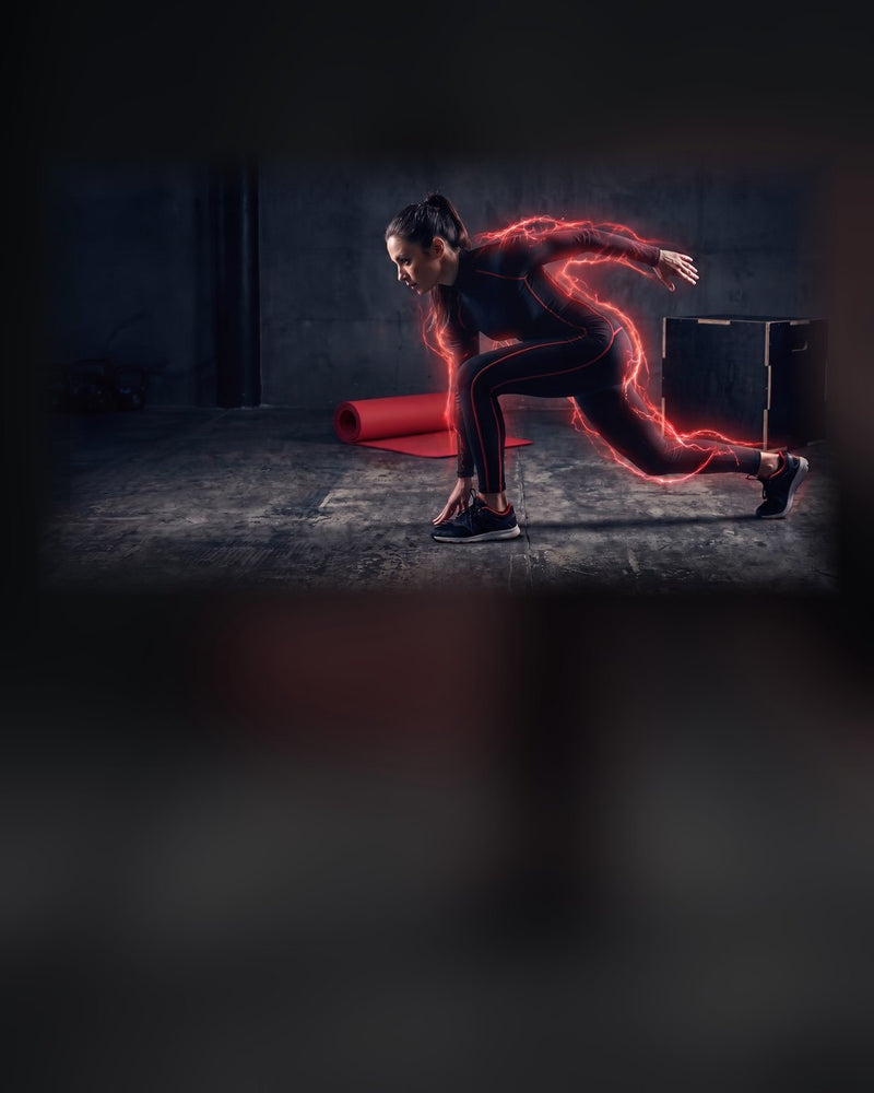 A woman driving out of a sprint start in a dark gym, trailed by red light, beside a rolled red mat and a plyo box.